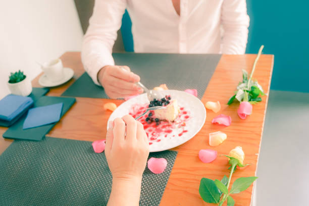Cheesecake with cranberry sauce on white plate. Couple eating sweet cake for anniversary or San Valentin. Focus on hand - Image