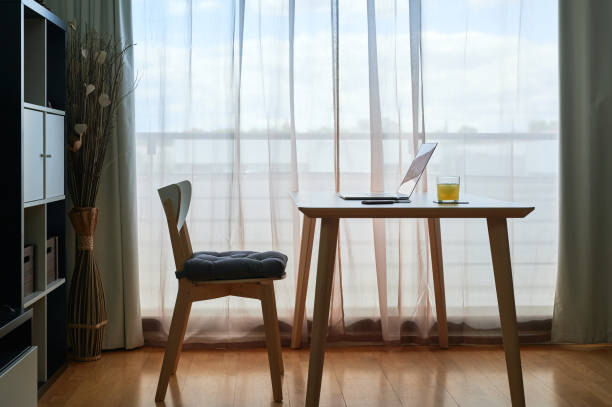 istock Simple but elegant empty home workspace with a wooden table with a laptop and a drink next to a large window 1319265535