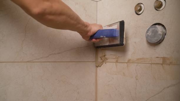 istock Close-up side view of a builder applying tiles and spacers between tiles that have been securely applied to the adhesive on the wall. master tiler glues wall white ceramic tiles. The master is laying the tiles in the bathroom. 1319265824