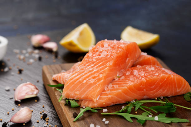 filete crudo de salmón con sal marina, limón y pimienta sobre fondo de piedra negra. - salmon fotografías e imágenes de stock