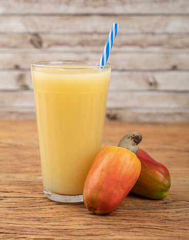Cashew juice in a glass with fruits over wooden table.