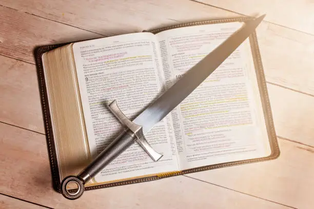 Photo of A Bible with a Sword on a Bright White Wooden Table