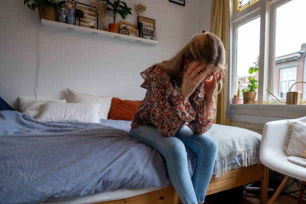 sad young woman is sitting on her bed