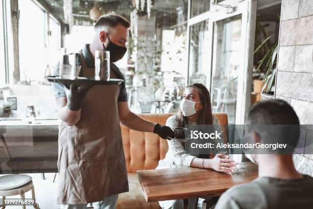 Couple With Face Mask Receiving Coffee And Refreshment From Waiter In Coffee Bar Stock Photo - Download Image Now