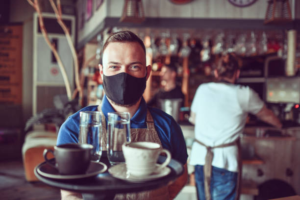 istock Modern Handsome Waiter Smiling Under Face Mask While On The Job 1319277749