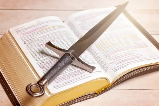A Bible with a Sword on a Bright White Wooden Table