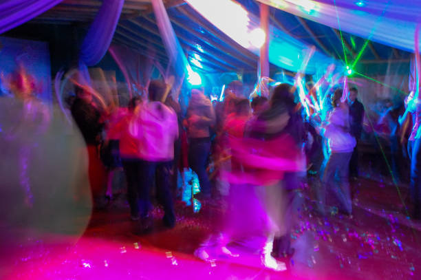 dance party in motion at night. Dancing crowd on the dance floor of a party blurred. Young people having fun at a celebration or event. Long exposure nightlife.