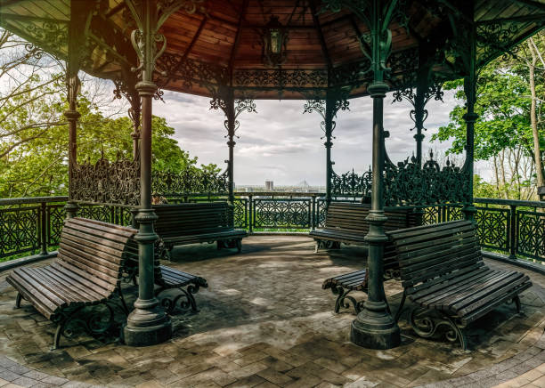 Arbor in a park with a sloping roof standing in the shade of trees with green grass around. A good place to relax outdoors.