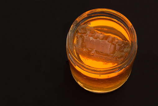 glass container, with honey and a piece of honeycomb. backlight on black background.