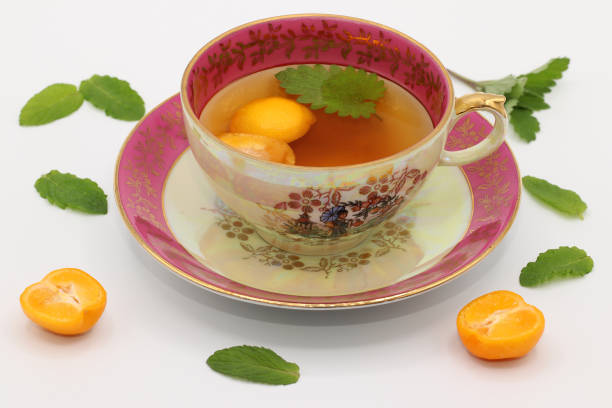 uma linda xícara de chá de porcelana vintage com uma folha melissa e fatias de calamansi. folhas de hortelã e metades de frutas de calamondin estão por aí. - five oclock tea - fotografias e filmes do acervo