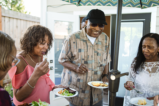 A large multi-generational group of family relatives enjoys takeout BBQ food in the backyard having not seen each other for a long time, due to normal circumstances or perhaps COVID-19 or Coronavirus.  Happiness and joy abound as they are together again.