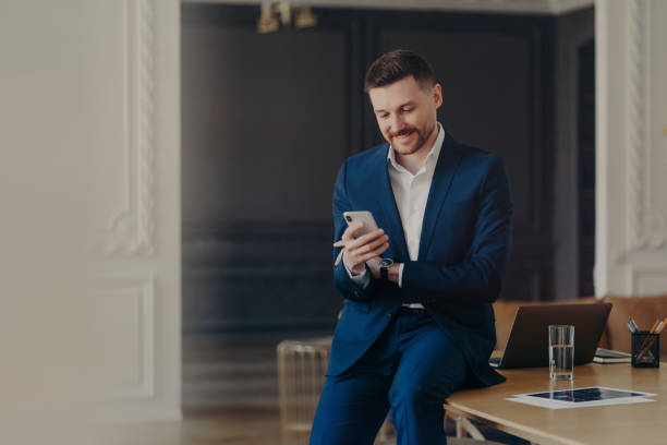 istock Happy handsome businessman looking at mobile phone while sitting on office desk 1319296614