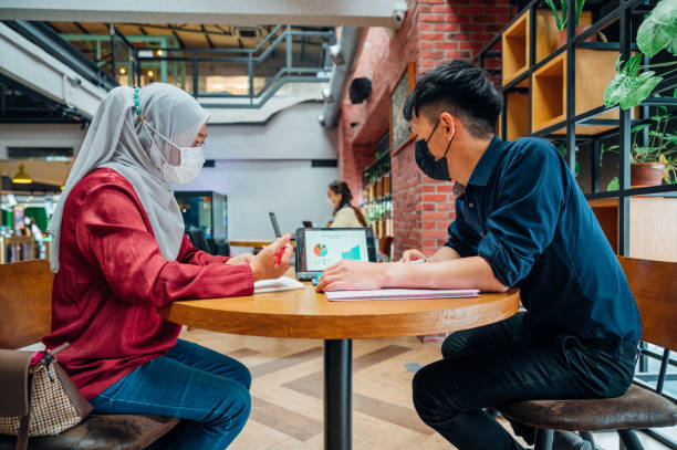 istock Coworkers with protective face masks looking at graph and talking about business strategy at office 1319296793