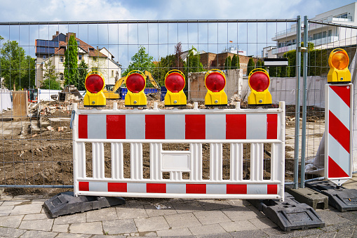 Red and white plastic portable barrier in front of a construction site. Red signal lights. Excavator in the background.