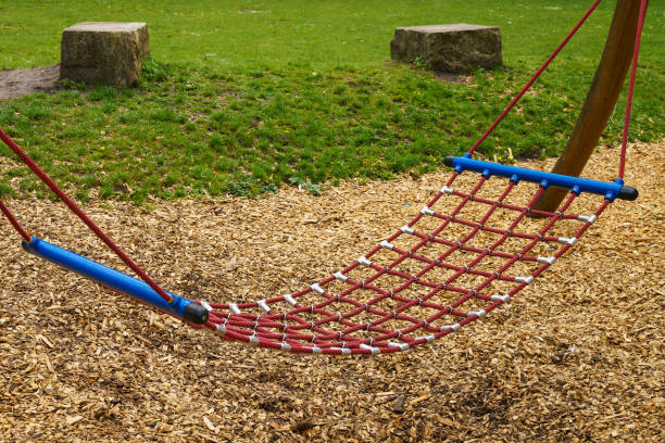 A relaxing rope hammock in the playground. Green lawn and two cubic stones.
