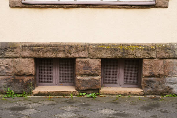 два окна подвала в каменной стене, покрытой металлической сеткой. - paving stone stone brick wall стоковые фото и изображения