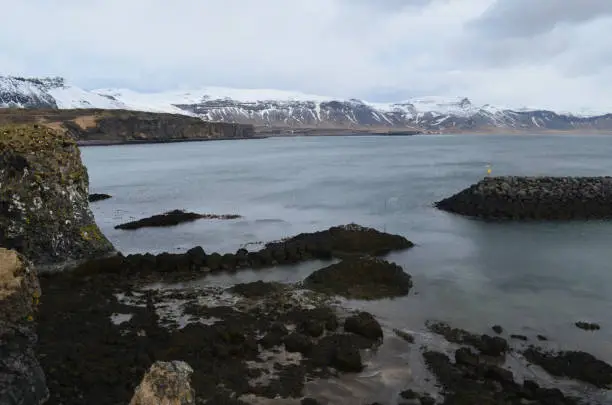 Snow capped mountains surrounding the rock coast of Hellnar Iceland.