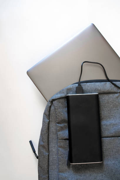 istock Gray textile backpack with a silver laptop or ultrabook and a large capacious power bank on a white background. The concept of recharging gadgets while traveling or trip 1319300356