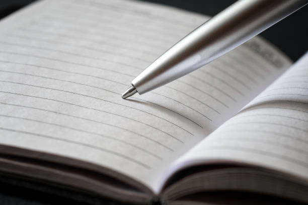 istock A silvery ballpoint pen writes in a lined notebook on a black background. Concept for creativity, writing a letter or book, study or office work. Macro 1319300379