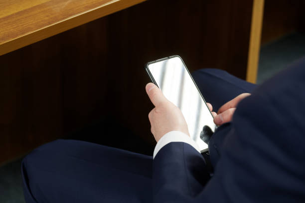 mężczyzna używa smartfona ukrytego pod stołem podczas spotkania, negocjacji, spotkania biznesowego lub lekcji. polityk, prawnik, urzędnik lub nauczyciel. bez twarzy - hiding internet multimedia people zdjęcia i obrazy z banku zdjęć