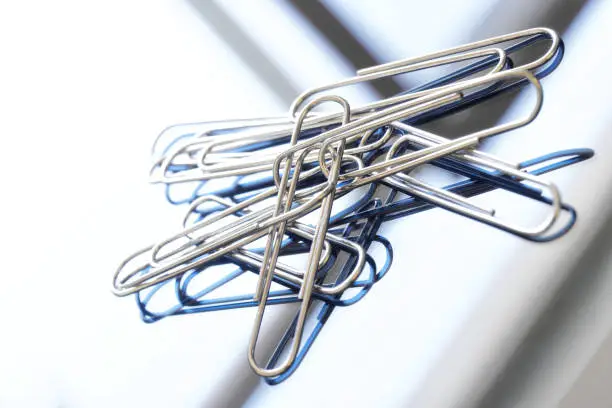 Photo of A pile of metal stationery with a paper clip on a reflective surface. Concept for neat office work. Macro. Selective focusing