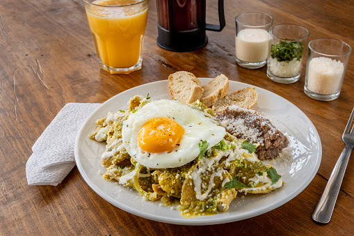 Mexican traditional chilaquiles breakfast Green red salsa Orange juice wooden