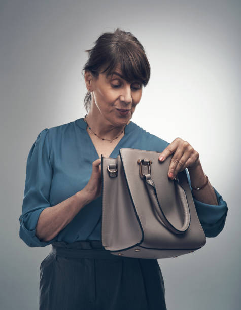 Studio shot of a senior woman looking for something in her handbag against a grey background What business move will she pull out of her bag today? older woman purse stock pictures, royalty-free photos & images