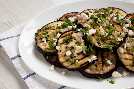 Homemade Grilled Eggplant with Feta and Herbs on a white plate on cloth, low angle view. Close-up.