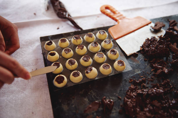 istock Confectioner hands putting chocolate filling into spherical molds from white chocolate and preparing chocolate truffles at home kitchen 1319305726