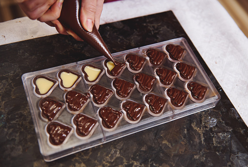 Top view of chocolatier squeezing filling of creamy liquid preparing luxury handmade chocolate pralines at home kitchen. Closeup