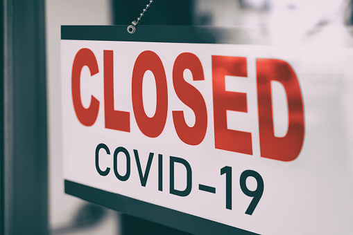 COVID Closed Sign hanging in window storefront. Government mandatory shutdown order of restaurants, non essential stores or curfew forcing closure of businesses leading to unemployment. Coronavirus