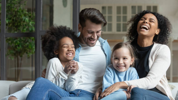 felice famiglia multirazziale con piccole figlie rilassarsi a casa - multi ethnic family foto e immagini stock