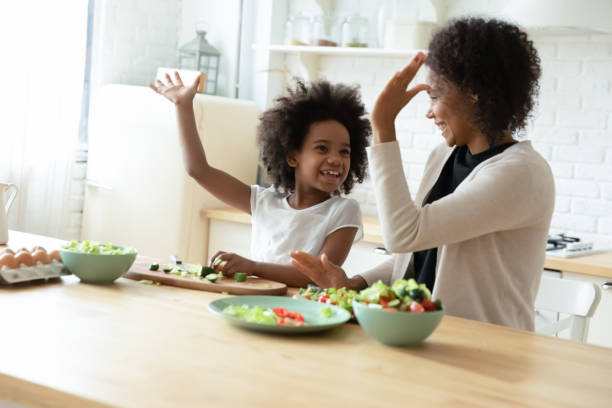 Happy African American mom and daughter give high five cooking
