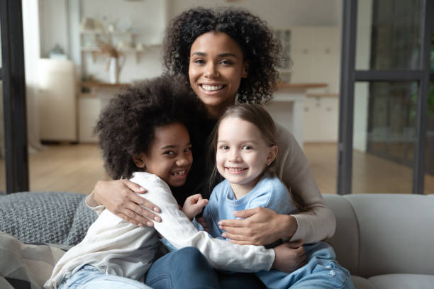 Portrait of biracial mom relax with multiethnic daughters Family portrait of African American mom sit on sofa at home relax with multiethnic daughters. Smiling biracial young mother rest on couch with diverse multiracial girls children. Adoption concept. foster care stock pictures, royalty-free photos & images