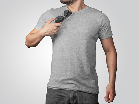 Mock up of male model wearing a heather gray t-shirt holding sun glasses on clear gray background.