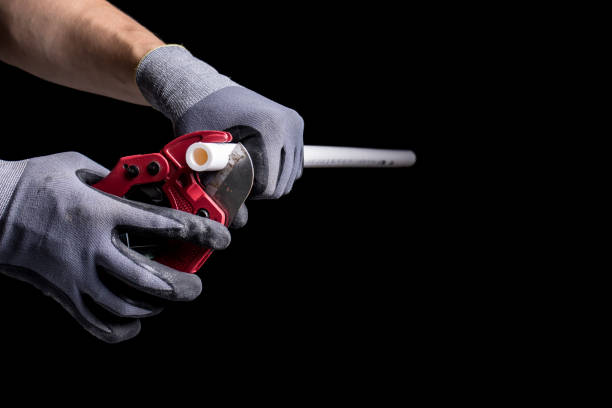 istock Hands of a plumber in gloves cutting a plastic pipe with a special tool. 1319318260