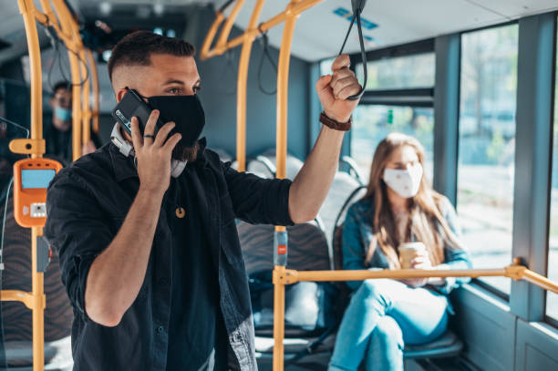 man wearing protective mask and using a smartphone while riding a bus - bus riding public transportation businessman imagens e fotografias de stock