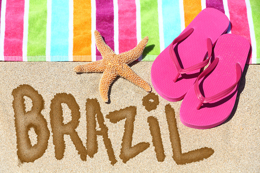 Brazil concept. Overhead view ot the word BRAZIL written on beach sand with a colorful striped towel, pink thongs and a starfish conceptual of a summer vacation and travel in Rio de Janiero, Brazil.