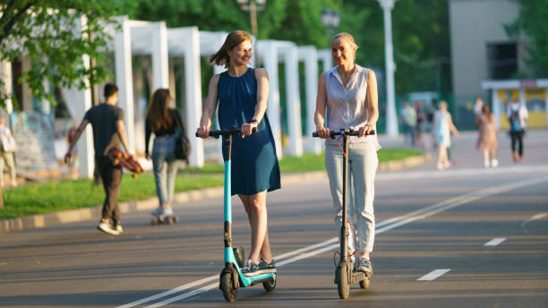 Sport activity in the public park Moscow, Russia - May 18, 2021: People in the public Gorky park in spring hot day. Leisure theme. Two young women riding electric motorised scooters. Frontal view. They are happy moscow stock pictures, royalty-free photos & images