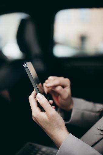 Close-up shot of businesswoman working with her smartphone inside the car.