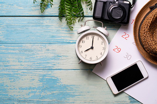 concept of travel plan with alarm clock, calendar, mobile phone, camera for vacation trip planning on blue wooden table background