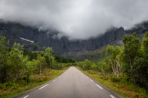 Empty road leading to a rocky mountain covered with clouds near the village of Nusfjord in the Lofoten Islands during summer.