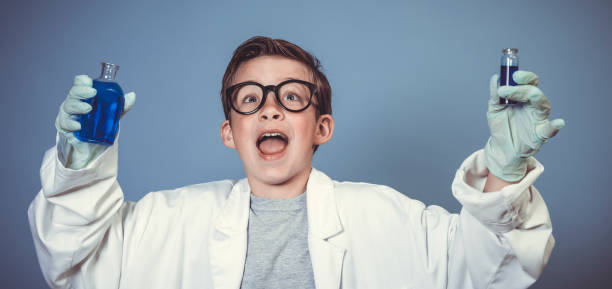 fajny chłopiec szkolny z grubymi czarnymi okularami jest przebrany za naukowca z białym płaszczem i eksperymentuje z niebieskimi płynami - doctor male white scientist zdjęcia i obrazy z banku zdjęć