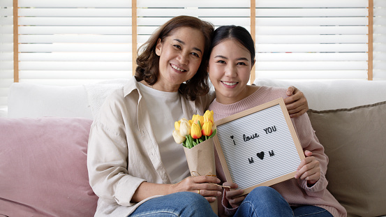 Portrait attractive beautiful mum sit with daughter give gift photo frame and flower in family moment celebrate look at camera. Overjoy bonding cheerful kid embrace relationship with retired mom.