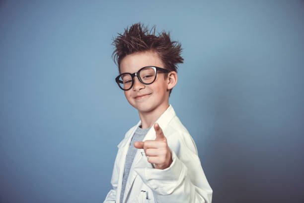 cool school boy with thick black glasses is dressed as mad scientist with white coat in front of blue background