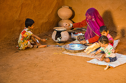 Jaisalmer, rajasthan, india - april 18th, 2018: Rural women cooking in her house and feeding her children, poor family concept.