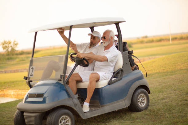 두 명의 나이든 친구가 골프 카트를 타고 있습니다. - senior couple golf retirement action 뉴스 사진 이미지