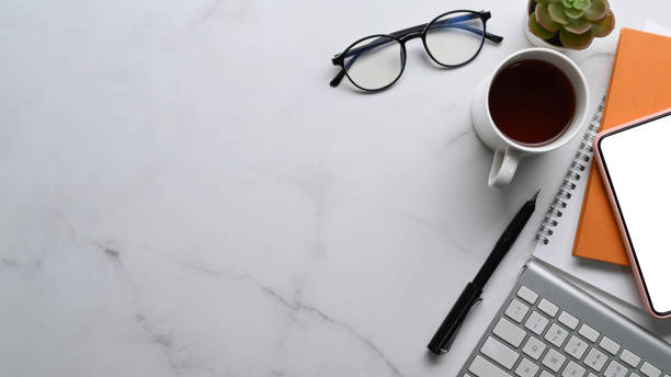 istock Top view of simple workspace with notebook, glasses, coffee cup and smart phone on marble background. 1319375736