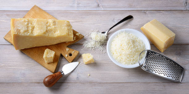 pezzi di parmigiano e grattugiati su sfondo legno con tagliere, coltello e grattugia. vista dall'alto. - food and drink cheese grated bowl foto e immagini stock