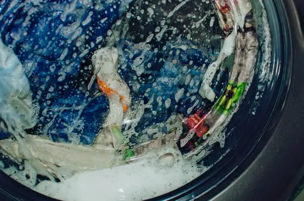 Photo of Closeup of washing machine full of dirty clothes. Laundry washing process.